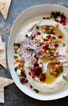 hummus with onions, chickpeas and garnish in a bowl next to tortilla chips