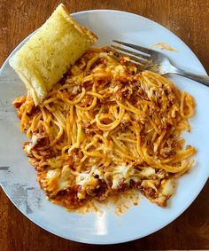 a white plate topped with spaghetti next to a piece of bread on top of a wooden table