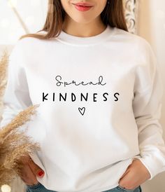 a woman wearing a white sweatshirt with the words spread kindness printed on it in black