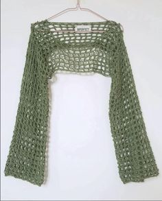 a green crochet top hanging on a white wall with a hanger in front of it