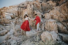 a man and woman in red dress standing on rocks