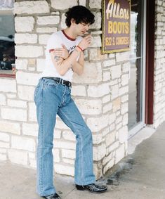 a man leaning against the side of a building with his hands on his hips and looking down