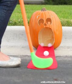 a person standing next to a fake pumpkin with its mouth open and tongue out on the ground