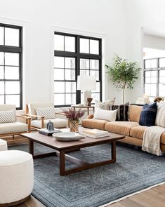 a living room with couches, chairs and tables in front of three large windows