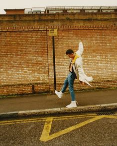 a man walking across a street next to a brick wall