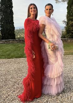 two women standing next to each other wearing dresses with feathers on the bottom and sides