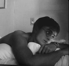 black and white photograph of a man in glasses laying on a bed with his arms crossed