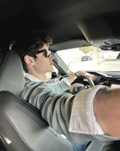 a young man driving a car with his hand on the steering wheel and wearing sunglasses