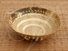 a gold colored bowl sitting on top of a woven tablecloth with an intricate design