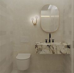 a white toilet sitting next to a sink in a bathroom under a round shaped mirror