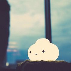 a small white cloud sitting on top of a table next to a person standing in front of a window