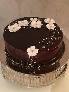 a chocolate cake with white flowers on top sitting on a silver platter in front of a wall