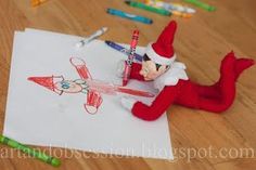 an elf is sitting on top of a piece of paper with crayons next to it