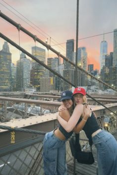 two women hugging each other while standing on a bridge in front of the city skyline