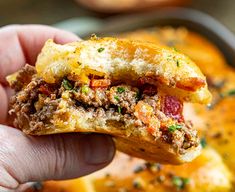 a hand holding a half eaten sandwich in front of a casserole dish filled with meat and cheese