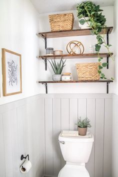 a white toilet sitting in a bathroom next to a wooden shelf filled with potted plants