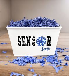 a white flower pot filled with blue flowers on top of a wooden table next to confetti