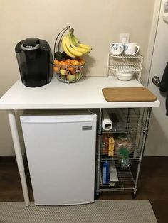 a small kitchen area with a refrigerator, coffee maker and fruit basket