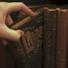 a person is holding an open book in front of two books on a shelf with other books behind them