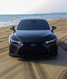 the front end of a black sports car parked on top of a sandy beach next to the ocean