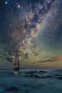 a boat floating on top of the ocean under a sky filled with lots of stars