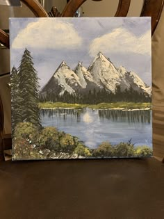 an acrylic painting of mountains and trees on a table with a lake in the foreground