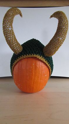 a knitted pumpkin with horns on it's head sitting on a wooden table