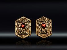 two gold earrings with red stones in the center and an intricate design on each side