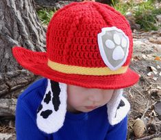 a small child wearing a red fireman hat with paw prints on the brim