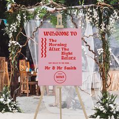 a pink sign sitting on top of a wooden easel next to flowers and greenery