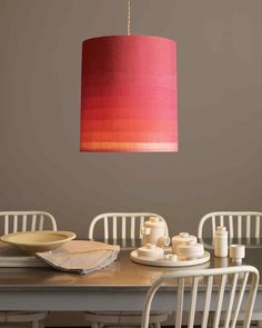 a red lamp hanging over a dining room table with white chairs and plates on it