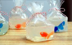 three bags filled with clear liquid and small goldfish decorations on top of a wooden table