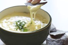 a person holding a tortilla chip and dipping it into a bowl of soup