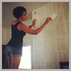 a woman standing in front of a white wall holding up a piece of paper with words on it