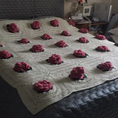 a crocheted blanket with pink flowers on it sitting on top of a bed