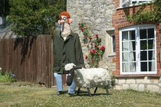 a man standing next to a sheep in front of a brick building with white windows