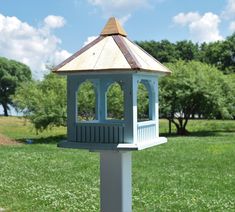 a blue and white bird house in the middle of a grassy field with trees behind it