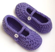 two purple crocheted baby shoes sitting on top of a white table