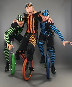 three men in circus costumes on bicycles posing for the camera