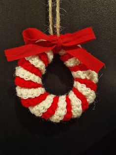 a red and white knitted wreath hanging from a string on a black surface with a red bow