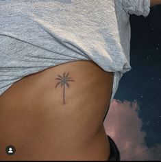 a woman's stomach with a small palm tree tattoo on the side of her belly