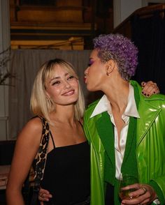 two women standing next to each other and one is wearing a green jacket with purple hair