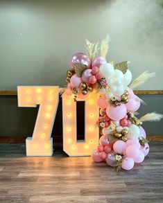 the number seventy is decorated with balloons and lights in pink, white and gold colors