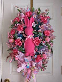 a pink bunny wreath with flowers and ribbons hanging on the front door to welcome guests