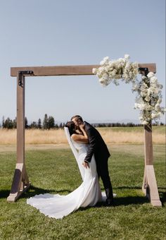 a bride and groom kissing in front of an outdoor ceremony arch with flowers on it