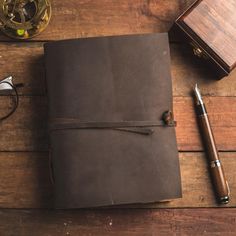 a brown leather journal sitting on top of a wooden table next to a pen and glasses