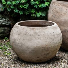 two large cement pots sitting on top of a gravel ground next to a green bush