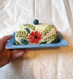 a hand holding a blue and white plate with a flower covered cake on it's side