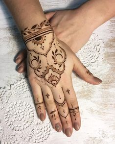 two hands with henna tattoos on them, one is holding the other's hand