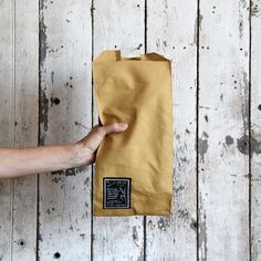 a hand holding a brown paper bag on top of a wooden floor next to a white wall